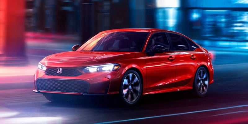 A bright red 2023 Honda Civic sedan drives forward on a dark road, illuminated by colorful streetlights.